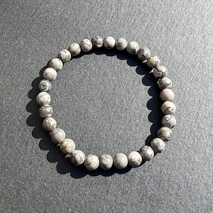 Peut inclure: Un bracelet de perles rondes, grises et blanches. Les perles sont ornées d'un motif marbré. Elles sont enfilées pour former un cercle. Ce bijou simple et élégant est parfait pour un usage quotidien.