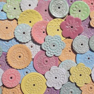 Könnte beinhalten: Sortiment an bunten Keramik-Ornamenten mit filigranen Designs. Die Ornamente sind rund und haben ein Loch in der Mitte. Sie sind perfekt, um jedem Raum einen Hauch von Verspieltheit zu verleihen.