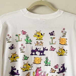 May include: White t-shirt with a colorful graphic print of various animals in a playful, cartoon style. The animals include dogs, cats, birds, and snakes.