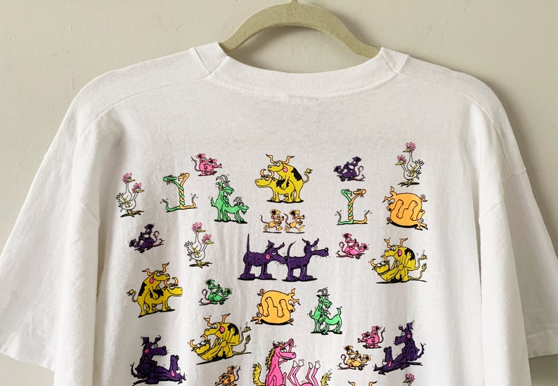 May include: White t-shirt with a colorful graphic print of various animals in a playful, cartoon style. The animals include dogs, cats, birds, and snakes.