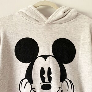 Puede incluir: Una sudadera con capucha gris claro con un gr&aacute;fico de Mickey Mouse en blanco y negro en la parte delantera.
