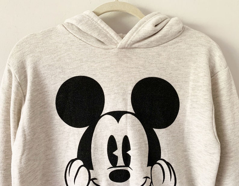 Puede incluir: Una sudadera con capucha gris claro con un gr&aacute;fico de Mickey Mouse en blanco y negro en la parte delantera.
