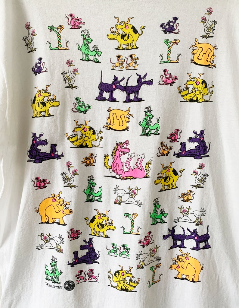 May include: White t-shirt with a colorful graphic print of various animals in different positions. The animals include pigs, cows, dogs, snakes, and birds. The print is a repeating pattern and covers the entire shirt.
