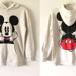 Puede incluir: Una sudadera con capucha gris con un gr&aacute;fico de Mickey Mouse en blanco y negro en la parte delantera y un gr&aacute;fico de Mickey Mouse en blanco y negro con orejas rojas en la parte posterior.