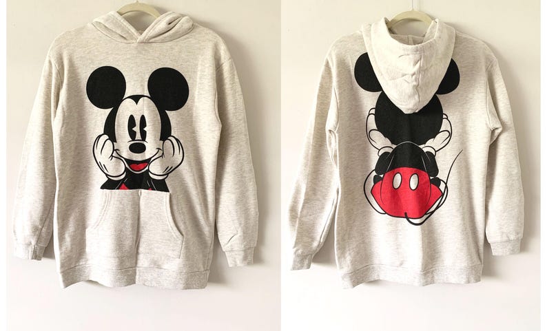 Puede incluir: Una sudadera con capucha gris con un gr&aacute;fico de Mickey Mouse en blanco y negro en la parte delantera y un gr&aacute;fico de Mickey Mouse en blanco y negro con orejas rojas en la parte posterior.