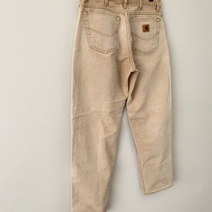 Puede incluir: Un par de pantalones vaqueros Carhartt de color marr&oacute;n claro con un parche de cuero marr&oacute;n en el bolsillo trasero.