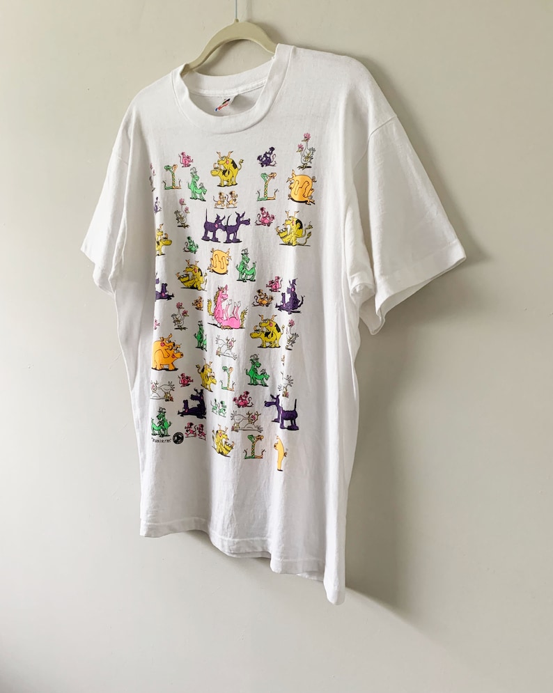 May include: White t-shirt with a colorful cartoon print of various animals. The animals are all different colors and have different expressions. The shirt is a vintage style and has a crew neck.