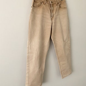 Puede incluir: Un par de pantalones vaqueros de color marr&oacute;n claro colgados de una percha. Los vaqueros tienen una pierna recta y un ajuste holgado.