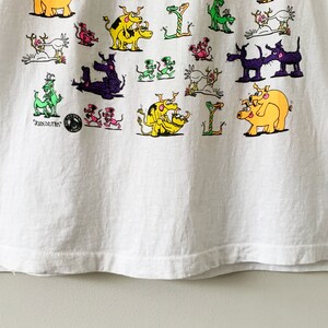 May include: White t-shirt with a colorful graphic print of various animals, including pigs, dogs, and dragons. The text "JUNKIES" is printed on the bottom left corner of the shirt.