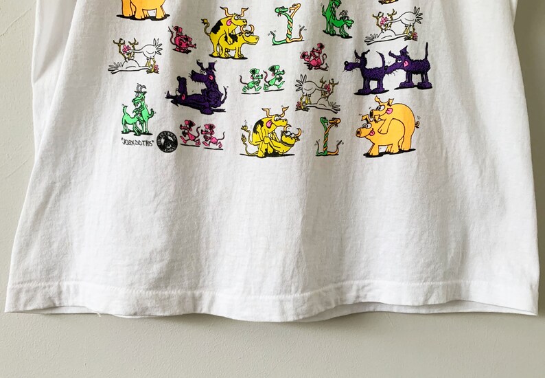 May include: White t-shirt with a colorful graphic print of various animals, including pigs, dogs, and dragons. The text "JUNKIES" is printed on the bottom left corner of the shirt.