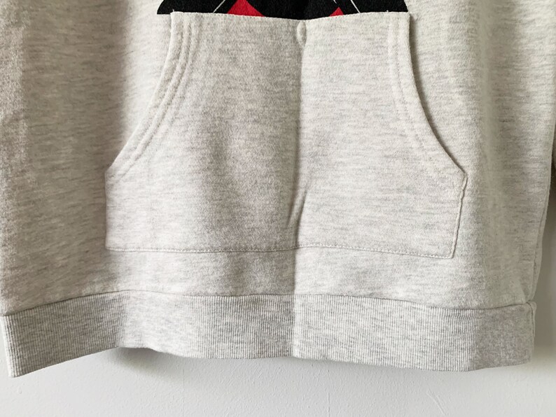 Puede incluir: Una sudadera con capucha gris con un bolsillo en la parte delantera. La sudadera tiene un dobladillo y pu&ntilde;os de canal&eacute;.