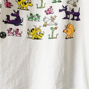 May include: White t-shirt with a colorful cartoon print of various animals, including snakes, pigs, dogs, and chickens. The text "YOU DO THIS" is printed on the bottom left corner of the shirt.