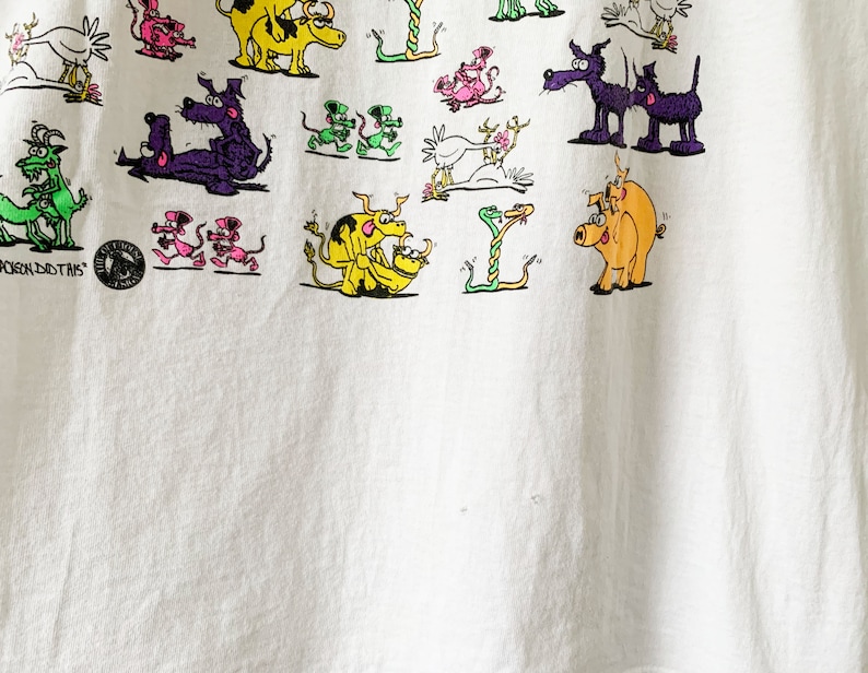May include: White t-shirt with a colorful cartoon print of various animals, including snakes, pigs, dogs, and chickens. The text "YOU DO THIS" is printed on the bottom left corner of the shirt.