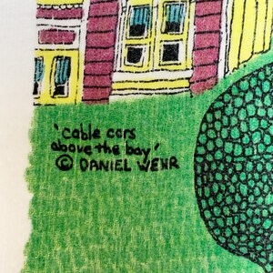 May include: A colorful illustration featuring a house with yellow trim and red walls, with the text "cable cars above the bay" and the artist's name, Daniel Wehr. The image is set against a green lawn.