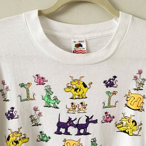 May include: White long-sleeve t-shirt with a colorful cartoon print of various animals, including snakes, birds, and dogs. The shirt has a Fruit of the Loom tag.