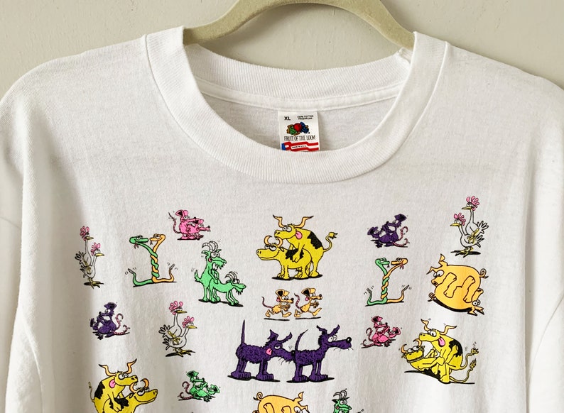 May include: White long-sleeve t-shirt with a colorful cartoon print of various animals, including snakes, birds, and dogs. The shirt has a Fruit of the Loom tag.