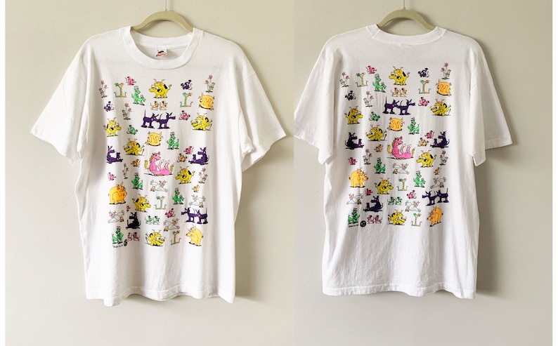 May include: White t-shirt with a colorful graphic print of various cartoon animals. The print features a variety of animals, including dogs, cats, and dragons, all in different colors and poses.