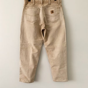 Puede incluir: Un par de pantalones vaqueros Carhartt de color marr&oacute;n claro con un parche de cuero marr&oacute;n en el bolsillo trasero.