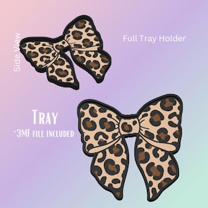 May include: Two leopard print bow-shaped tray holders. One bow is shown from the side view, and the other is a full view. The bows have a black outline and are tan with brown spots. The word "TRAY" is printed in white.