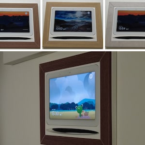 Peut inclure: Un cadre photo numérique blanc avec un cadre en bois brun est monté sur un mur. Le cadre affiche une image de dessin animé d'une grenouille sur une couverture de pique-nique. L'heure est 15h30.