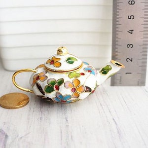 May include: A small white teapot with a gold handle and lid. The teapot is decorated with colorful floral designs in shades of blue, yellow, green, and pink.