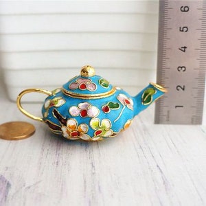 May include: A small blue teapot with a floral design. The teapot is made of metal and has a gold lid and handle.