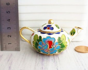 May include: A small white teapot with a gold lid and handle. The teapot is decorated with a floral design in blue, green, red, and gold.