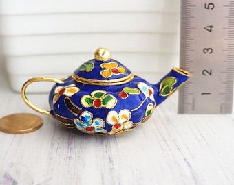 Puede incluir: Una pequeña tetera azul con una tapa dorada y diseños florales en tonos rojos, amarillos y blancos. La tetera está hecha de esmalte y tiene un diseño delicado y ornamentado.