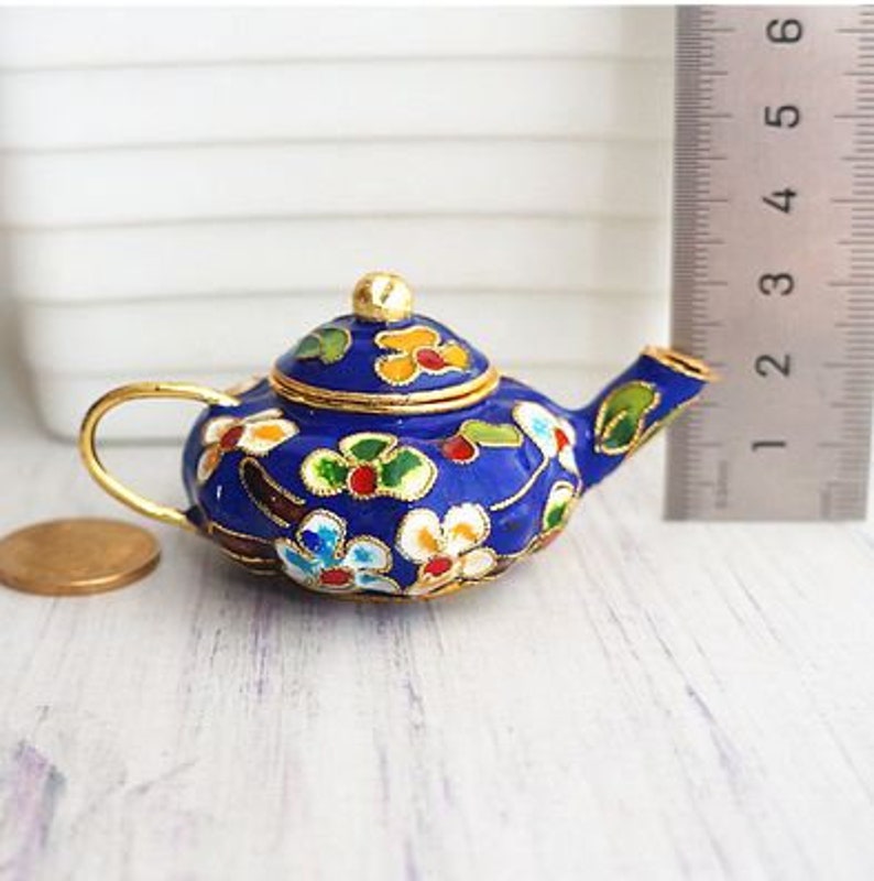 May include: A small blue teapot with a gold lid and floral designs in shades of red, yellow, and white. The teapot is made of enamel and has a delicate, ornate design.