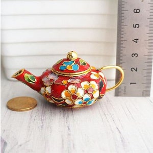 May include: A small red teapot with a gold handle and floral design. The teapot is decorated with white, blue, and gold flowers.