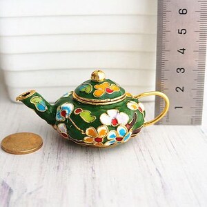 May include: A small green teapot with a gold lid and floral design. The teapot is decorated with colorful flowers and leaves.