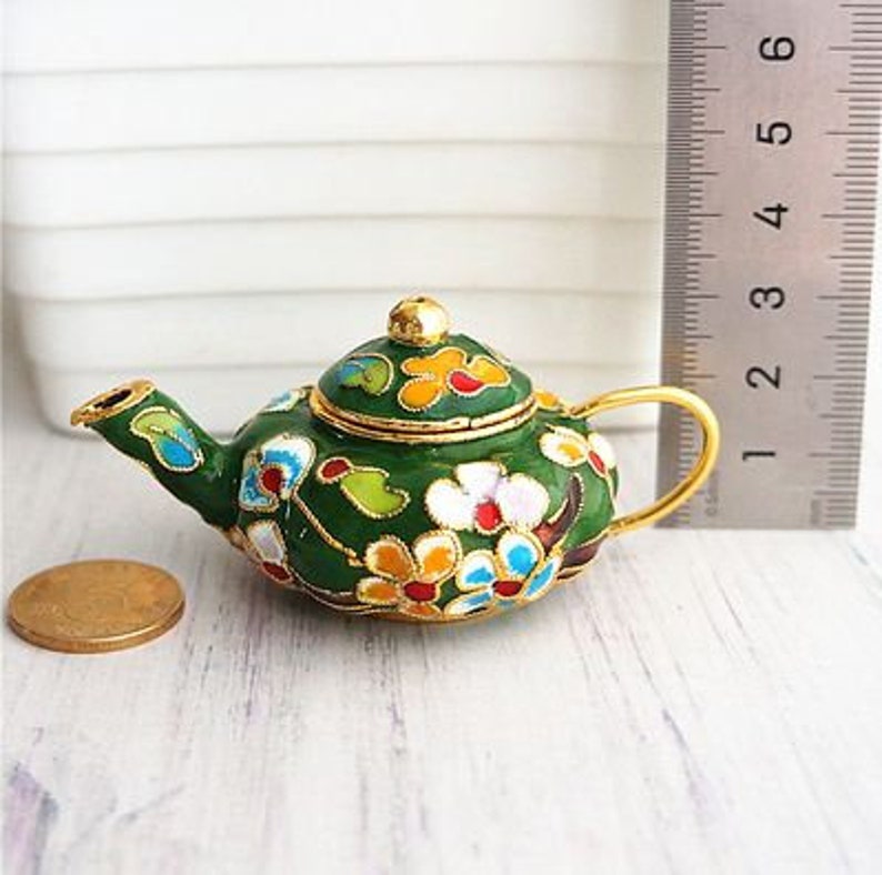 May include: A small green teapot with a gold lid and floral design. The teapot is decorated with colorful flowers and leaves.