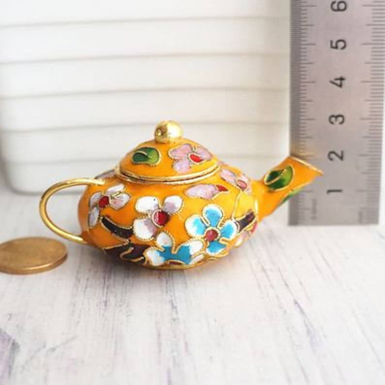 May include: A small, yellow teapot with a floral design. The teapot is decorated with pink, blue, green, and white flowers. The teapot has a gold handle and spout.