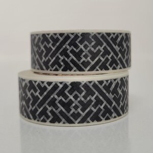 May include: Two rolls of black and white patterned washi tape. The tape has a geometric design.