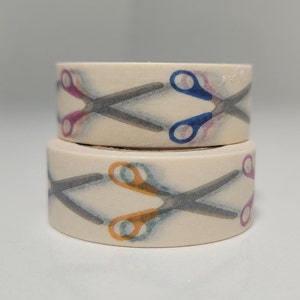 Puede incluir: Dos rollos de cinta washi con un patrón de tijeras en tonos de azul, rosa, naranja y gris sobre un fondo blanco.