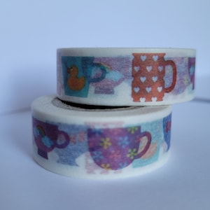 May include: Two rolls of washi tape with a white background and colorful designs of teacups and a rubber duck. The teacups have different patterns and colors, including purple, pink, blue, and orange.