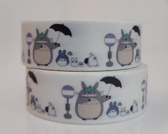 May include: Two rolls of white washi tape featuring a repeating pattern of a large gray creature with an umbrella, smaller creatures, and bus stop signs. The tape is designed for crafting and scrapbooking.