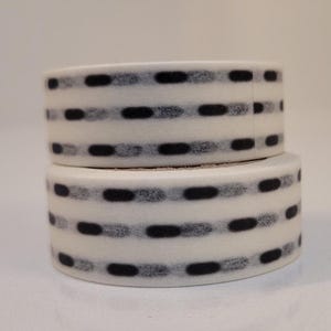May include: Two rolls of white washi tape with a black and gray striped pattern. The tape has a subtle dotted texture.