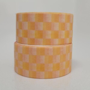 May include: Two rolls of washi tape with a checkered pattern in shades of orange and pink.