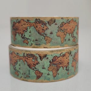 May include: Two rolls of decorative washi tape featuring a vintage world map design. The map is in shades of brown and green, with small boat illustrations. The tape is ideal for scrapbooking, journaling, or adding a travel theme to crafts.