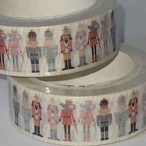 May include: A roll of washi tape with a repeating pattern of nutcracker and mouse characters. The tape is white with a gold glitter background.