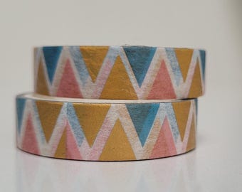 May include: Two rolls of decorative washi tape. Each roll features a repeating pattern of gold, light blue, and pink triangles. The tape is stacked on top of each other, with the top roll slightly angled.