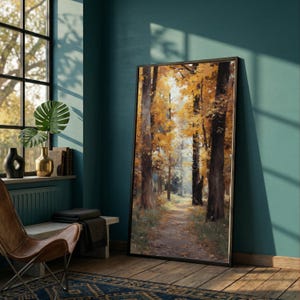 May include: A framed landscape painting shows a path through a forest with trees in autumnal colours. The artwork, in a black frame, leans against a teal wall. The scene evokes autumn. The painting is a decorative item.