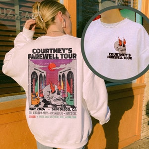 Puede incluir: Sudadera blanca con un estampado gráfico de una calavera con llamas y el texto "Courtney's Farewell Tour" en la espalda. La parte delantera de la sudadera tiene el mismo texto en una fuente más pequeña.