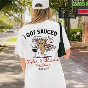 May include: White t-shirt with a graphic of a pizza slice with a face and the text "I got Sauced". The text "Tyler & Alicia's Wedding 12.31.2024" is printed below the graphic.