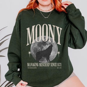 Könnte beinhalten: Ein dunkelgrüner Pullover mit einem Vintage-Grafikdesign. Das Design zeigt einen Wolf, der zu einem Vollmond heult, mit dem Text "Moony Managing Mischief Since 1971 The Marauders Est. 1971".
