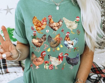 May include: A green t-shirt featuring a watercolor illustration of various chickens adorned with Santa hats and festive bows. The chickens are surrounded by Christmas-themed elements like presents and candy canes. The shirt is a relaxed fit.