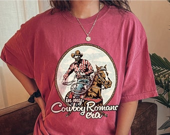Peut inclure: Un t-shirt rose surdimensionné avec un graphique représentant un cow-boy à cheval. Le graphique est dans un cercle avec le texte "in my Cowboy Romance era" en dessous.