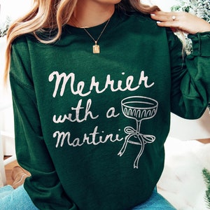 May include: A green sweatshirt with the text "Merrier with a Martini" in white lettering and a silver martini glass graphic.