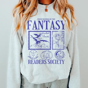 Op de afbeelding: Grijs sweatshirt met een blauwe grafische print die "Proud Member of the Fantasy Readers Society" zegt. De grafiek toont een draak, een roos, een boek en een maan.
